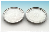 Matching round footed silver trays with Patterson family crest of a mother dragon with babies. Rim decorated with two scalloped bands. An interior etched decorative band surrounds the central motif.