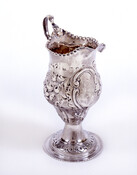 Cream pitcher with round base. Embellished with elaborate repoussé floral motif and gadrooned lip and spout. Medallion with engraved initials on front.