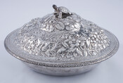Two-piece silver covered dish. Repoussé lid decorated with grass, dogs, flowers, lily pads, and a turtle finial. Plain base. Makers mark on bottom reads "Sterling A. Jacobi & Co. Baltimore."