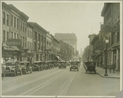 View of Charles Street looking south from Oliver Street (north of Mt. Royal Avenue) in Baltimore, Maryland. Shows Kruger's Hotel, Delphi Lunch Rooms, Hotel Plaza, New Lyceum, Belvedere Hotel, Cadillac, Western Union, and Ford, along with other businesses, automobiles and streetcar tracks. The Washington Monument is visible in the background.