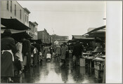 View of stalls and shoppers in the rain at Baltimore, Maryland's Belair Market, as seen looking east on Forrest Street at Gay Street.