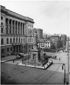 View of Battle Monument Square in Baltimore, Maryland, showing the Battle Monument, courthouse, and northwest side of the 300 block of Calvert Street. Pedestrians and horse-drawn carriages are visible around the monument and a streetcar can be seen in the background.