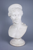 Sculptural bust of Lataetia Bonaparte (1750-1836), also known as Madame Mère. She is portrayed as a woman with curly hair tied back and parted in the middle, worn under a Roman headpiece. Her head is turned to the left.