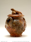 Brown ceramic sugar bowl with lid. Loop handles on either side. Decorated with floral pattern in relief. Three dimensional bird handle on lid.