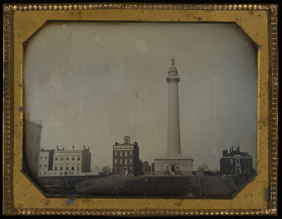 Early daguerreotype of the Washington Monument located in Mount Vernon Place of Baltimore, Maryland, potentially photographed by John Plumbe, Jr. Visible to the right of the monument are 2-8 (modern numbering) East Mount Vernon Place and to the left of the monument are 2, 8-10, and part of 12 West Mount Vernon Place.