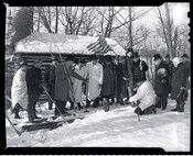 A group of men standing in the snow in front of a log cabin observing a groundhog on Groundhog Day at Slumbering Groundhog Lodge in Quarryville, Pennsylvania.