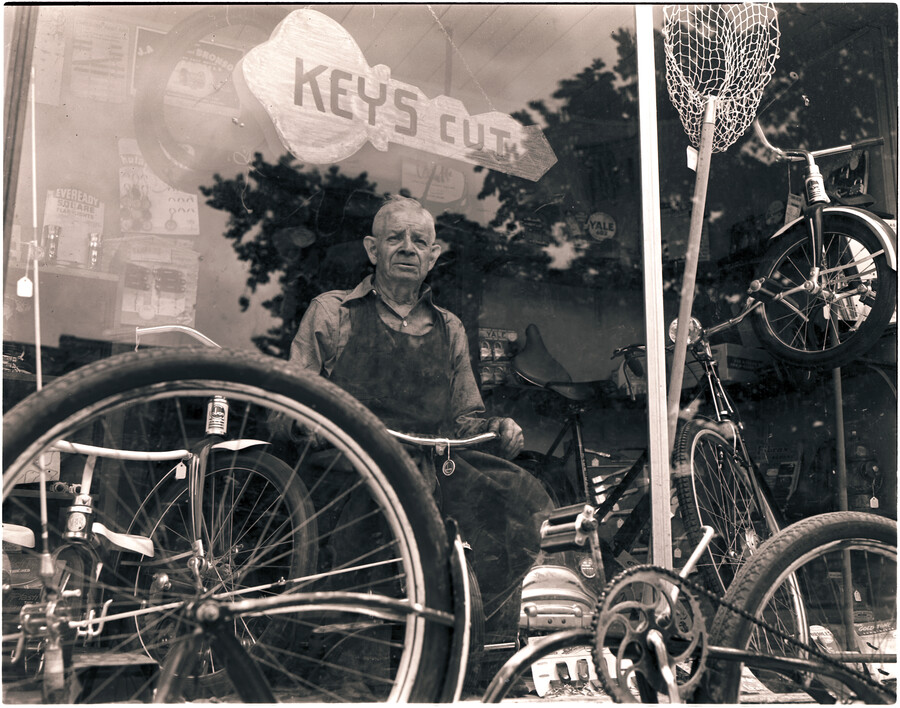 Bernard J. Logue standing in the window of his bicycle shop at 931 North Broadway, Baltimore, Maryland.