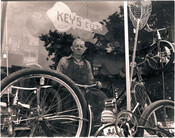 Bernard J. Logue standing in the window of his bicycle shop at 931 North Broadway, Baltimore, Maryland.